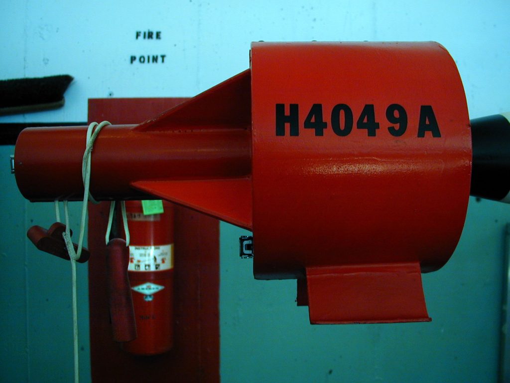 A red fire hose reel with the label "H4049A" mounted on a wall, next to a fire extinguisher and a "FIRE POINT" sign. 